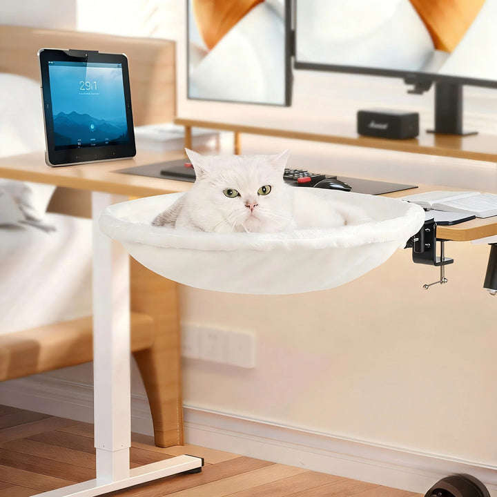Cat looking out from a plush white faux fur desk bed, a comfortable and elevated pet perch.