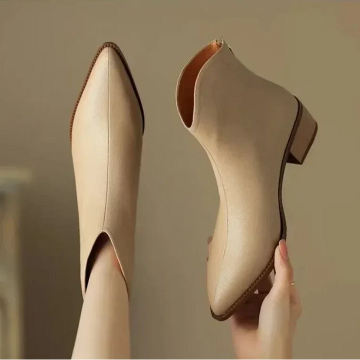 Women's pointed toe ankle boots paired with professional skirt for office wear. Sleek slip-on low heel style.