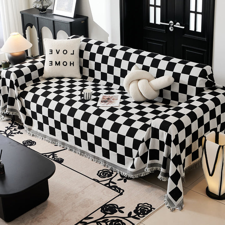 Checkerboard sofa blanket couch cover with fringe trim, made of polyester, draped over a living room sofa.