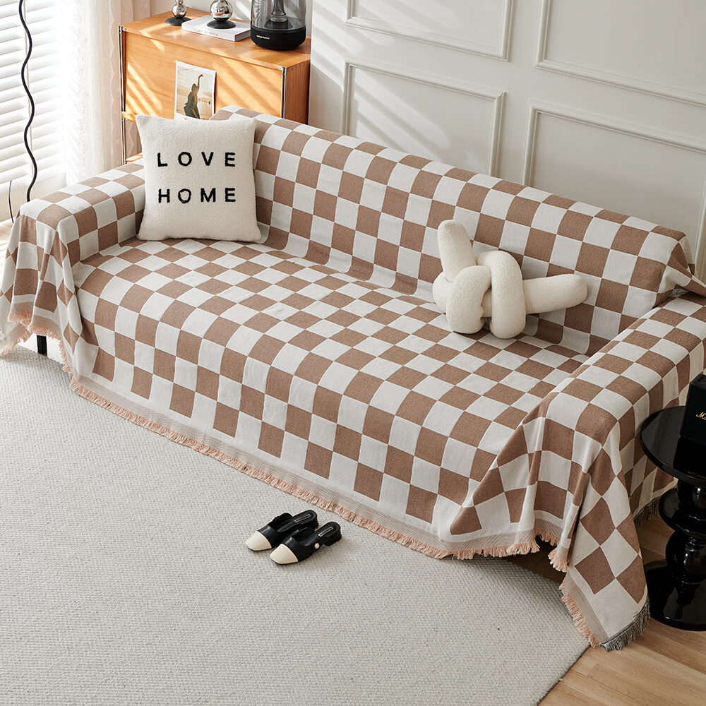 Stylish checkerboard patterned throw blanket with a fringe edge, used as a sofa cover in a modern living space.
