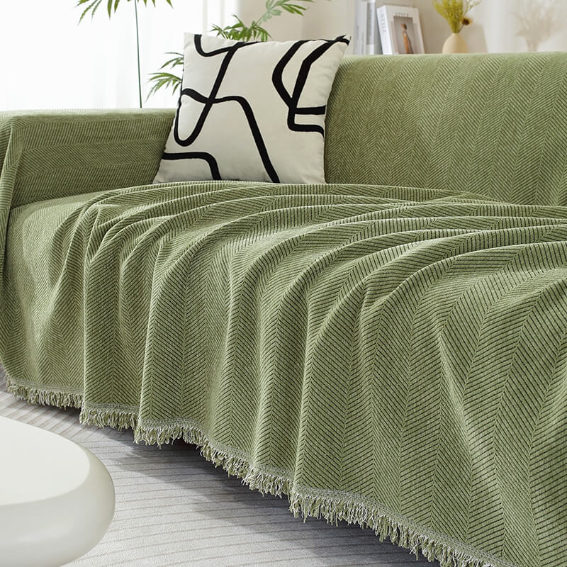 Chenille couch cover with herringbone pattern & decorative tassels, protecting sofa in living room