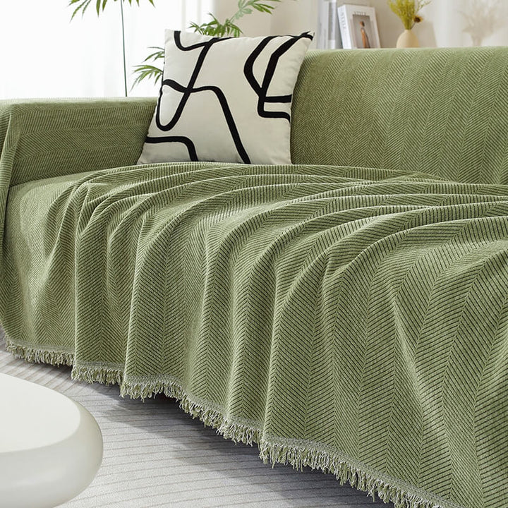 Chenille couch cover with herringbone pattern & decorative tassels, protecting sofa in living room