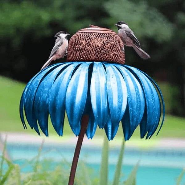 Decorative metal coneflower bird feeder with purple petals in a garden setting, attracting wild birds.