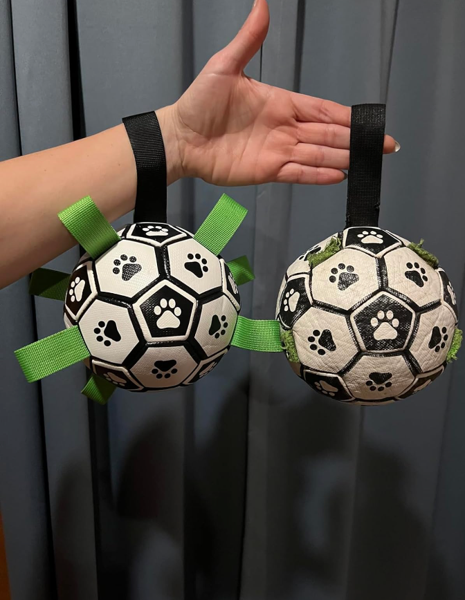 Interactive dog toy, black and white soccer ball with purple grab tabs, on green grass