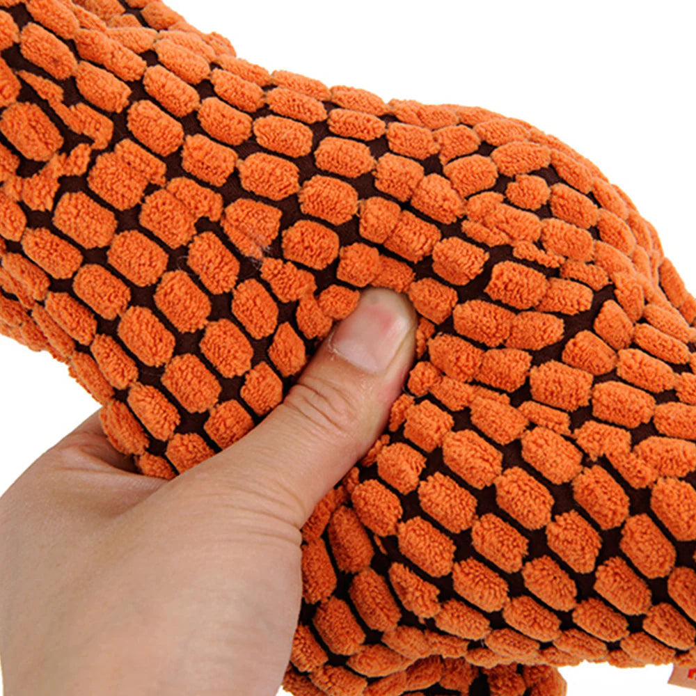 Indestructible plush dog toy with squeaker, perfect for strong chewers, laying on a dog bed.