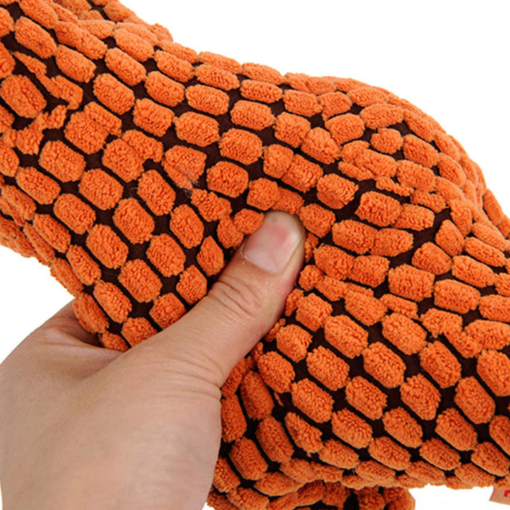 Indestructible plush dog toy with squeaker, perfect for strong chewers, laying on a dog bed.