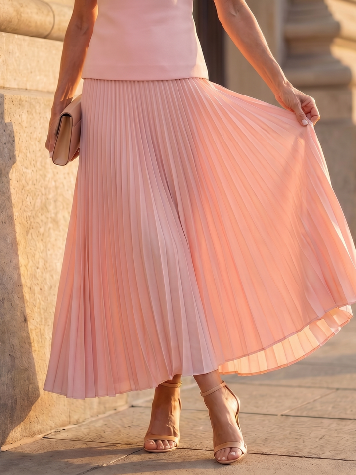 Full length view of a women's elegant pleated maxi skirt set with a structured sleeveless top.