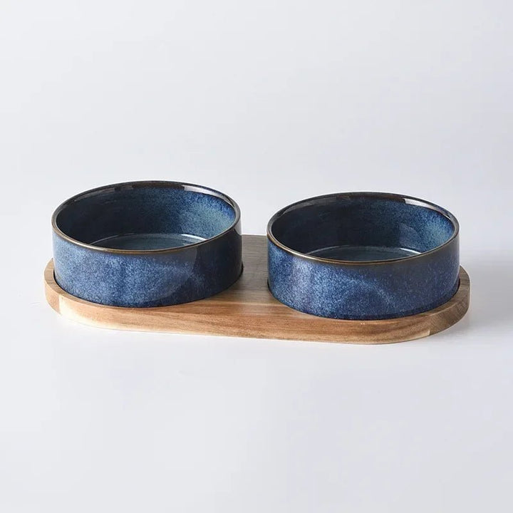 Two-piece pet feeding dish: a white ceramic bowl in a light-colored wooden ergonomic stand.