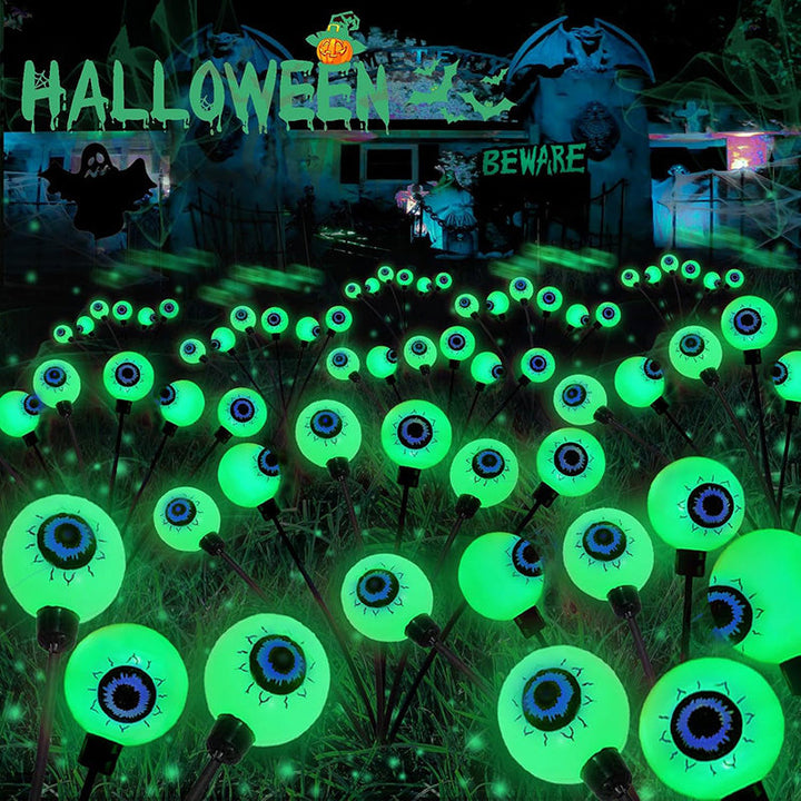 Close-up of a single solar eyeball light with a spooky red and green iris, glowing at night