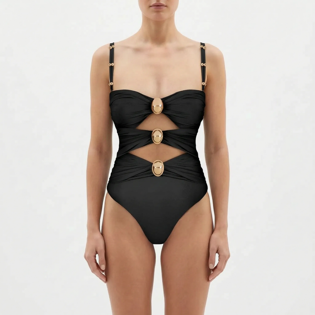 Woman in an elegant cutout one-piece swimsuit looking at the ocean during vacation.