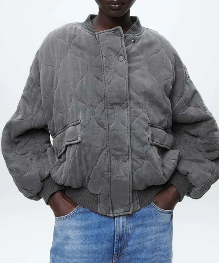 Close-up of a women's gray quilted bomber jacket featuring detailed stitching and ribbed cuffs. Winter coat.