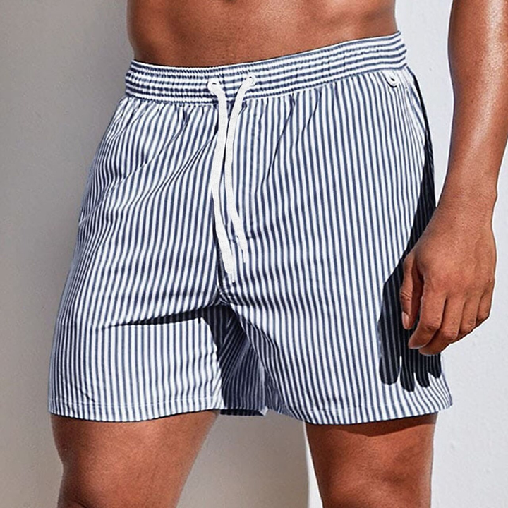 Man wearing striped quick-dry swim trunks, enjoying a sunny day at the beach.
