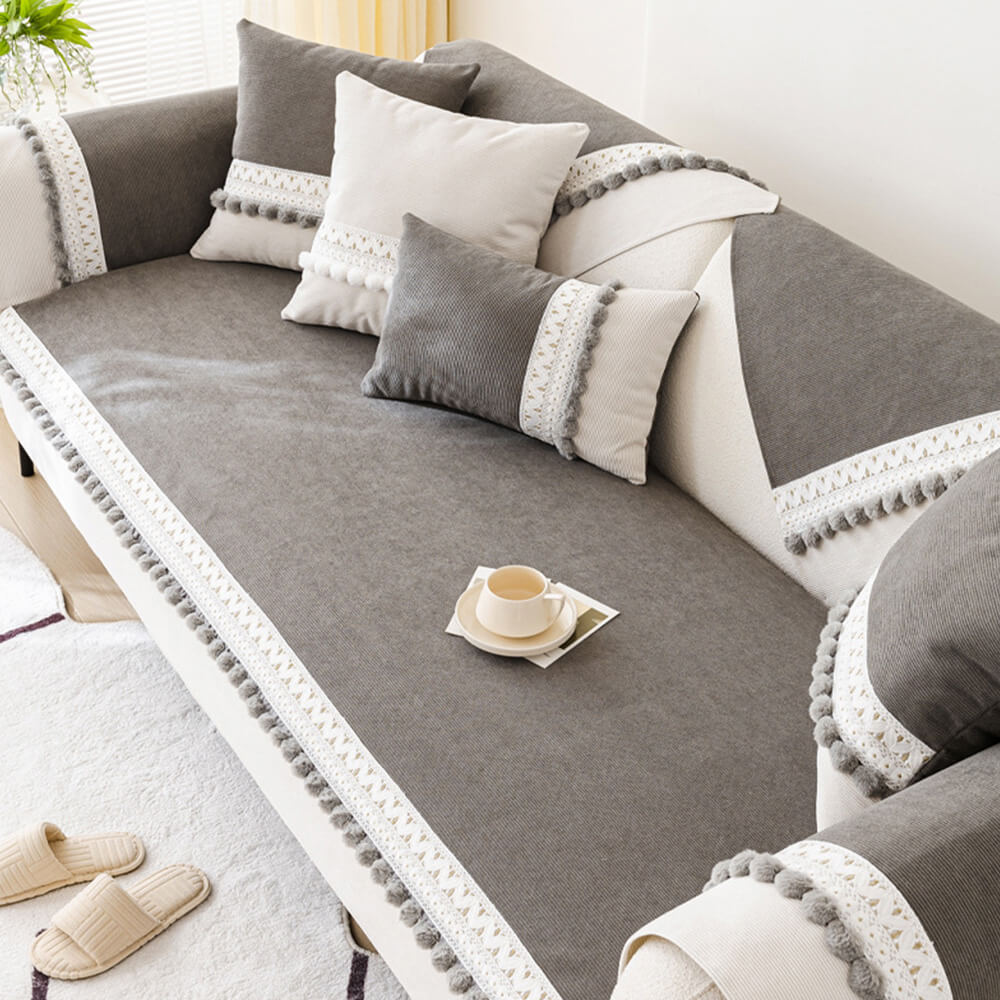Top-down view of a light grey corduroy sofa protector, highlighting its ribbed texture and pom-poms.