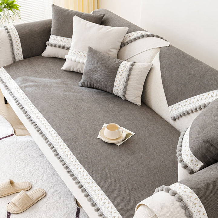 Top-down view of a light grey corduroy sofa protector, highlighting its ribbed texture and pom-poms.