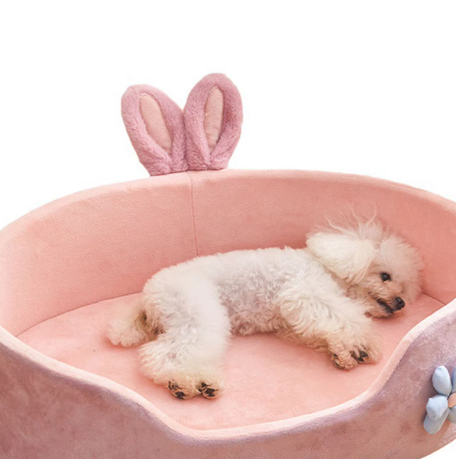 Warm pink pet bed adorned with playful bunny ears and a pretty flower, ideal for a resting pet.