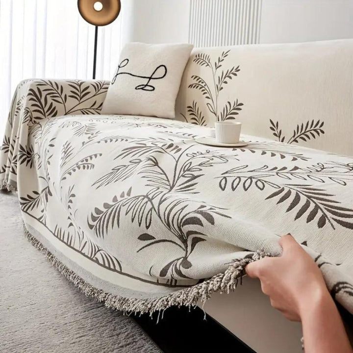 Beige chenille sofa cover with anti-slip backing and elegant tassel trim, protecting furniture.