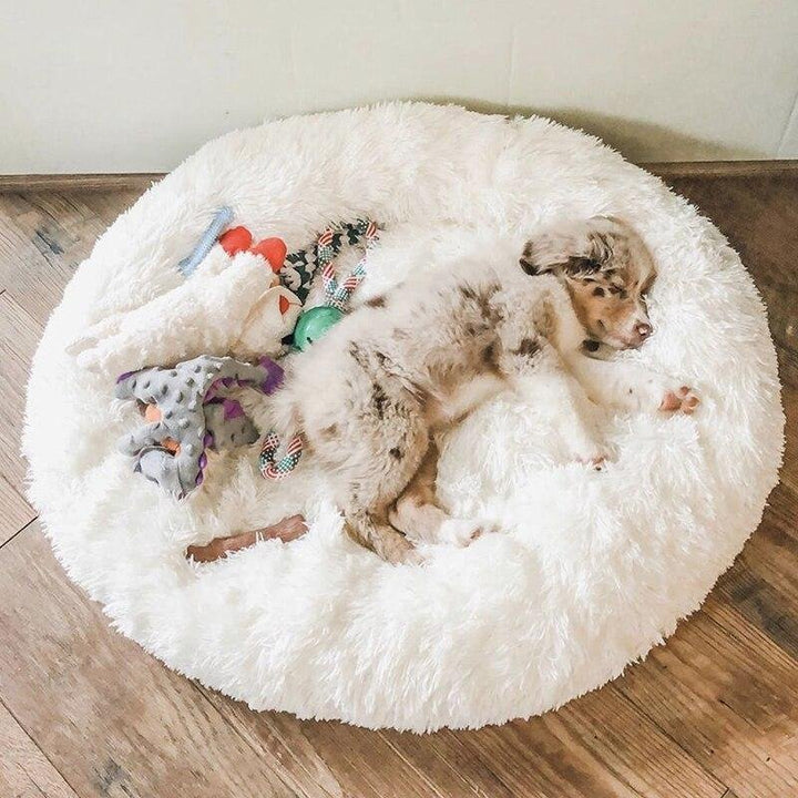 Beige faux fur calming pet bed, comfortable donut shape for anxious pets, aids deep sleep.