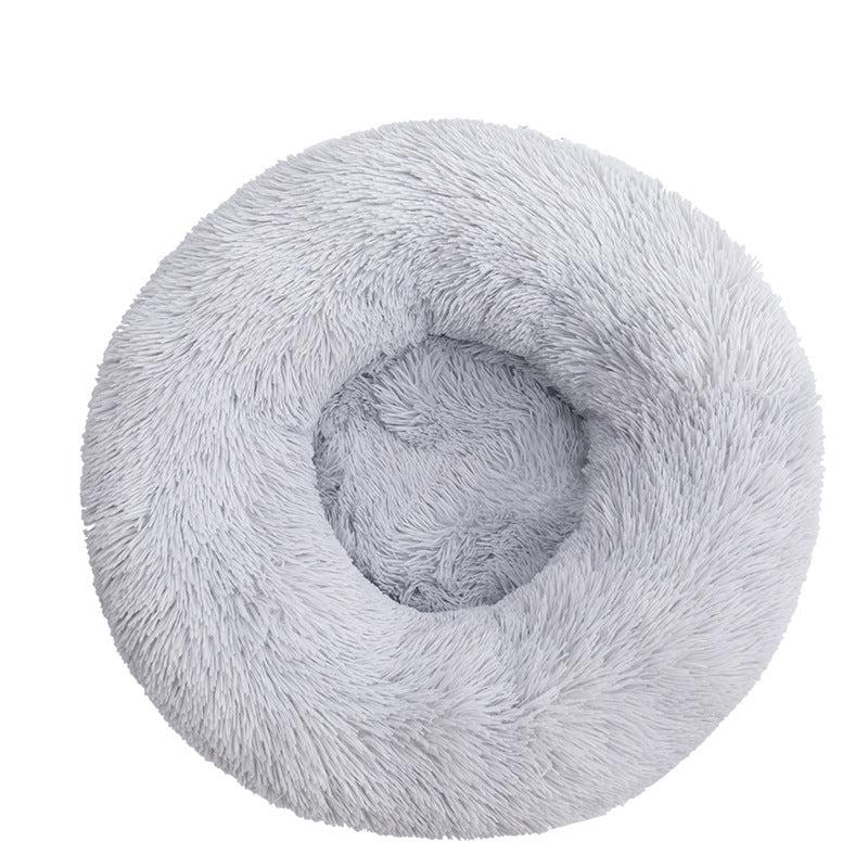 Elevated view of a round, soft calming pet bed in a home setting, grey color
