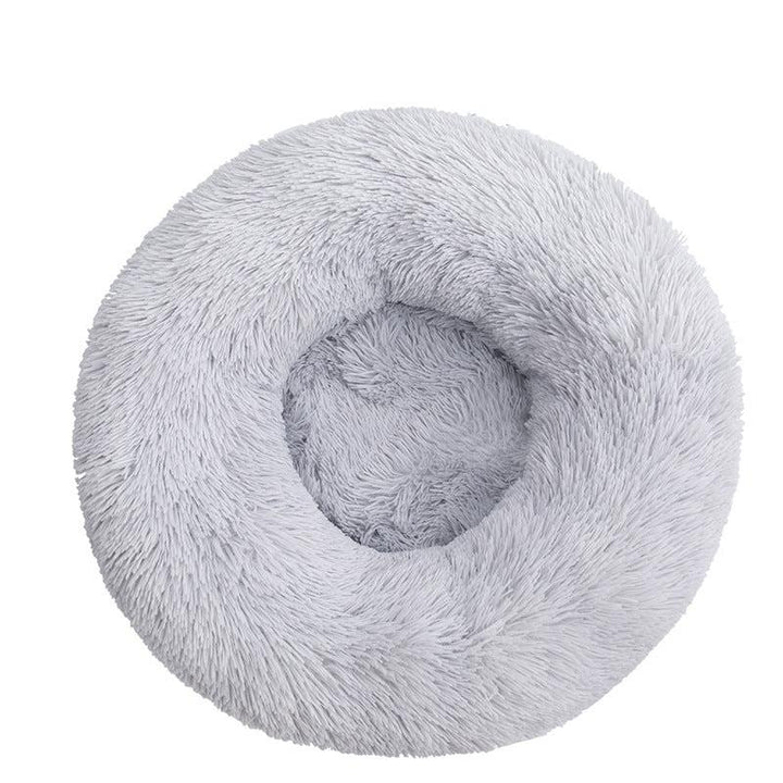 Elevated view of a round, soft calming pet bed in a home setting, grey color