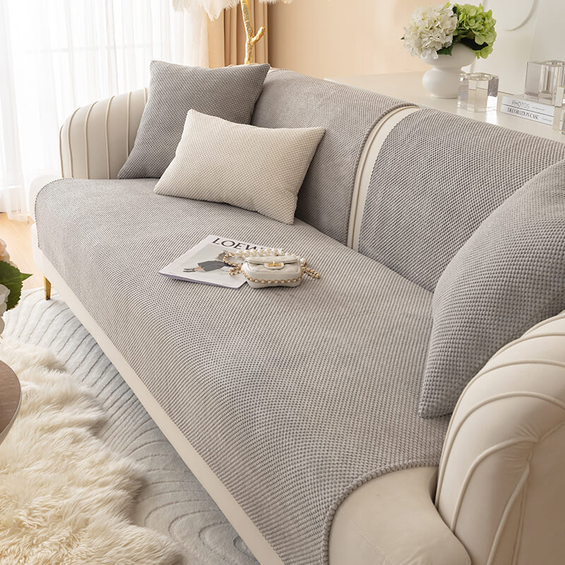 Plush solid color sofa cover draped over a three-seater couch, offering elegant furniture protection