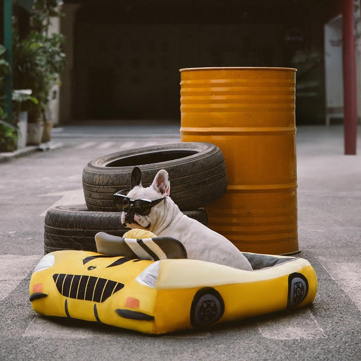 Small dog comfortably sleeping in a red race car pet bed with black and white checkered details.