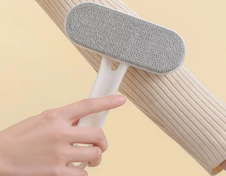 Hand holding a red reusable pet hair & lint remover roller over a dark fabric couch, showing use.