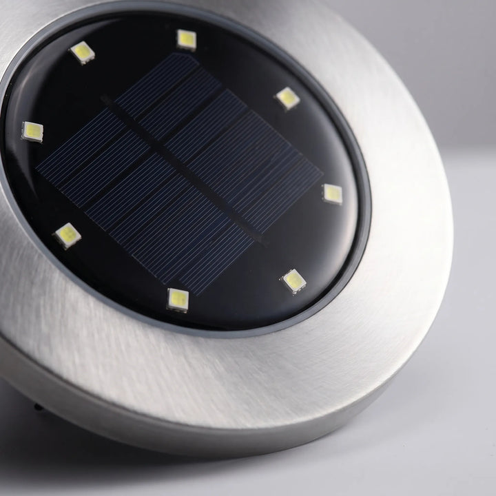 Round solar disk lights casting a bright glow on a garden pathway. Waterproof LED ground lights for outdoor landscaping.