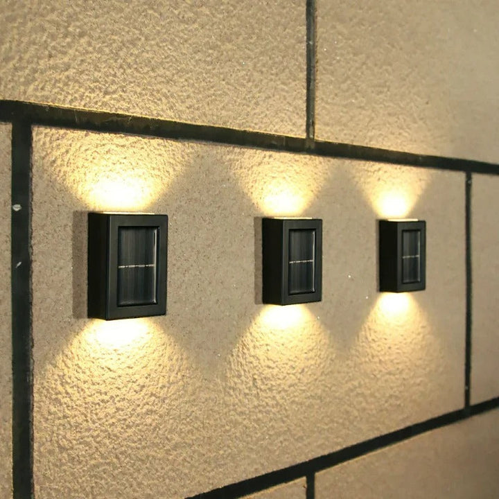 Modern solar LED wall lights mounted on an exterior wall, brightening a garden path at dusk. Wireless & energy-saving.