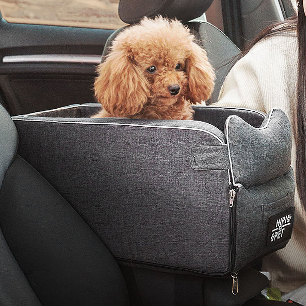 Small dog sitting happily in a grey suede pet lookout car seat on a car console.