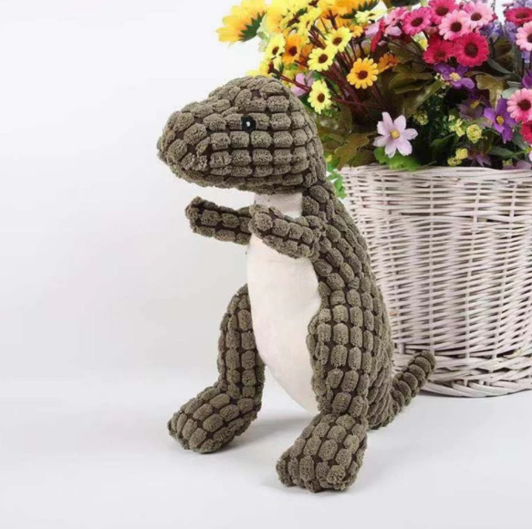Happy dog playing with a durable green dinosaur plush toy, an engaging pet supply