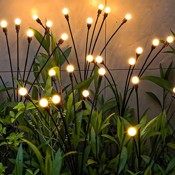 Multiple solar swaying firefly lights creating a magical starburst display in a green lawn at dusk.