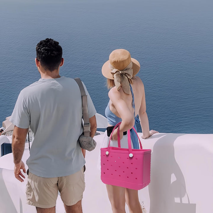 Person carrying a black unisex waterproof beach tote bag with drainage on a sunny day.
