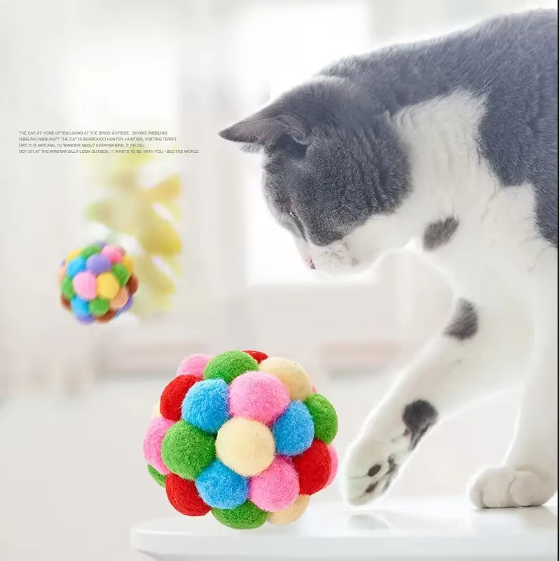 Vibrant multi-colored pompom cat toy ball on a wooden floor, soft interactive feline play.