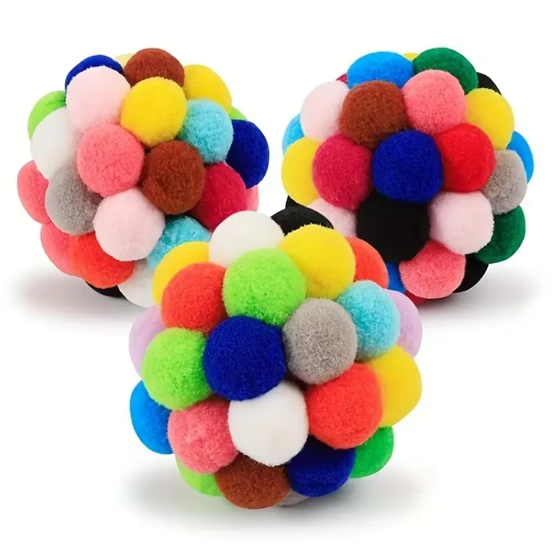 Hand holding out a fluffy, colorful pompom cat toy, emphasizing its soft texture for play.