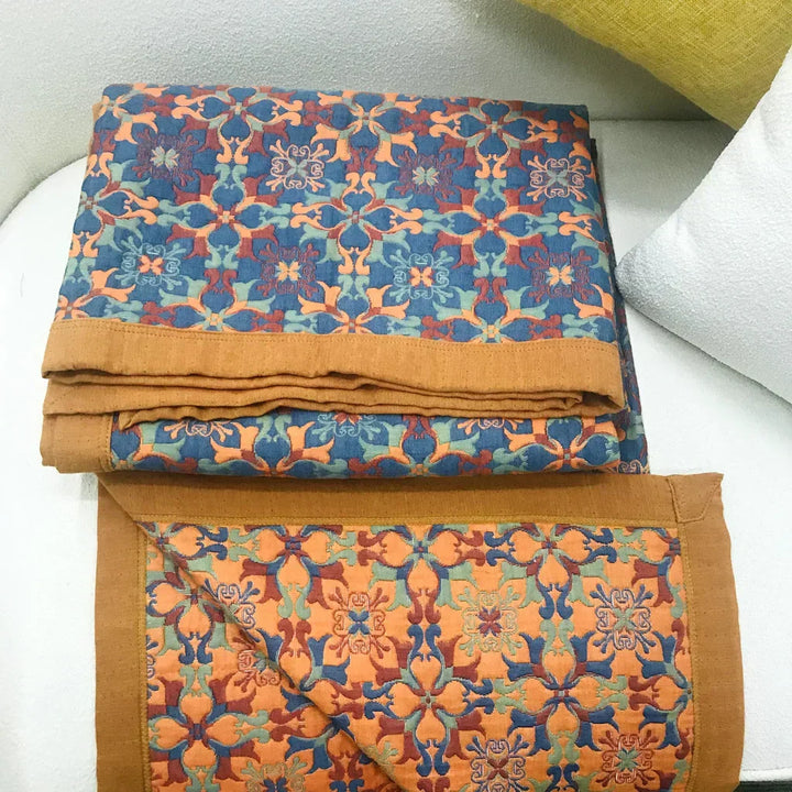 Top-down view of a vibrant orange & blue patterned six-layer cotton quilt. Reversible, cozy home bedding.