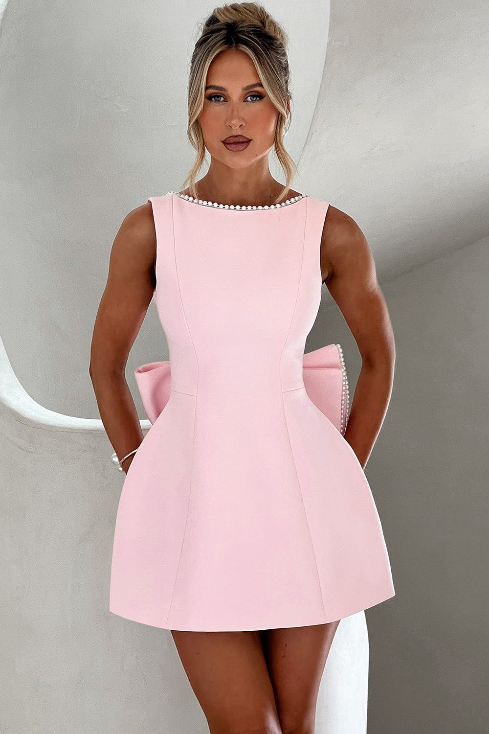 Women's A-line mini dress with delicate pearl trim and a striking statement back bow for parties.
