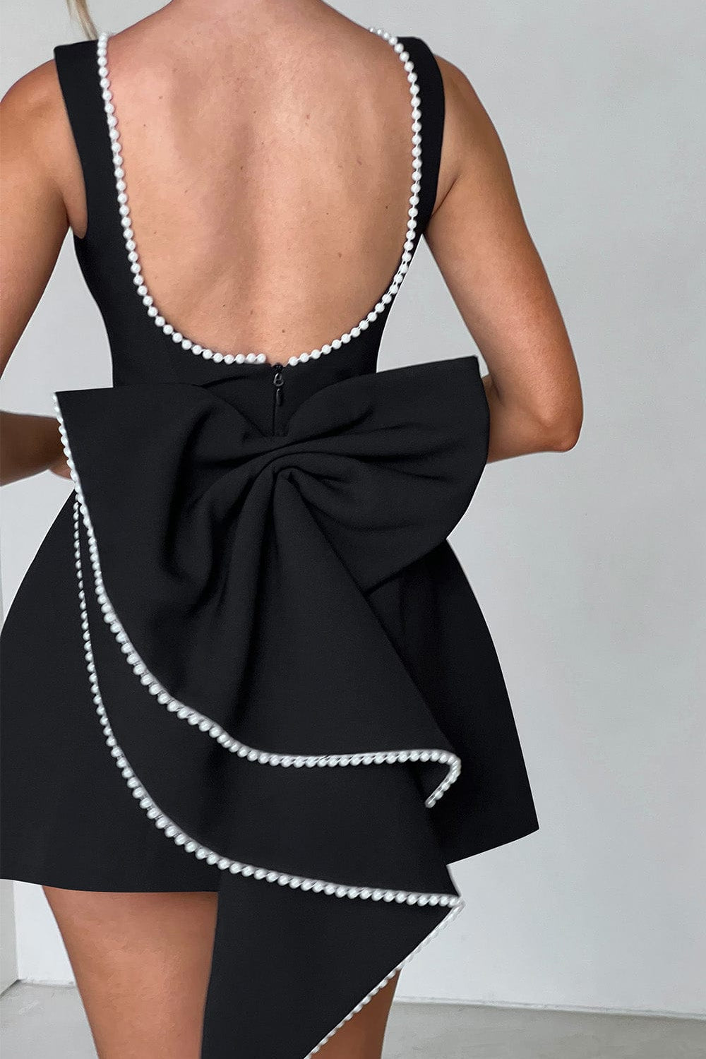 Backless women's cocktail dress, pearl trim mini with a striking statement back bow, perfect for celebrations.