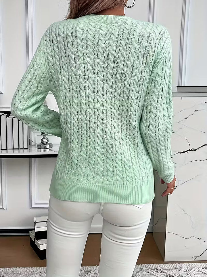 Close-up of intricate cable knit pattern on a women's crew neck sweater, showcasing classic knitwear.