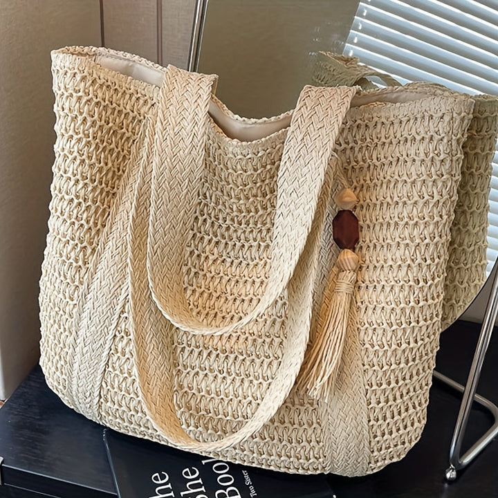 Elegant beige woven straw beach tote bag with decorative fringe tassel, a must-have vacation accessory.