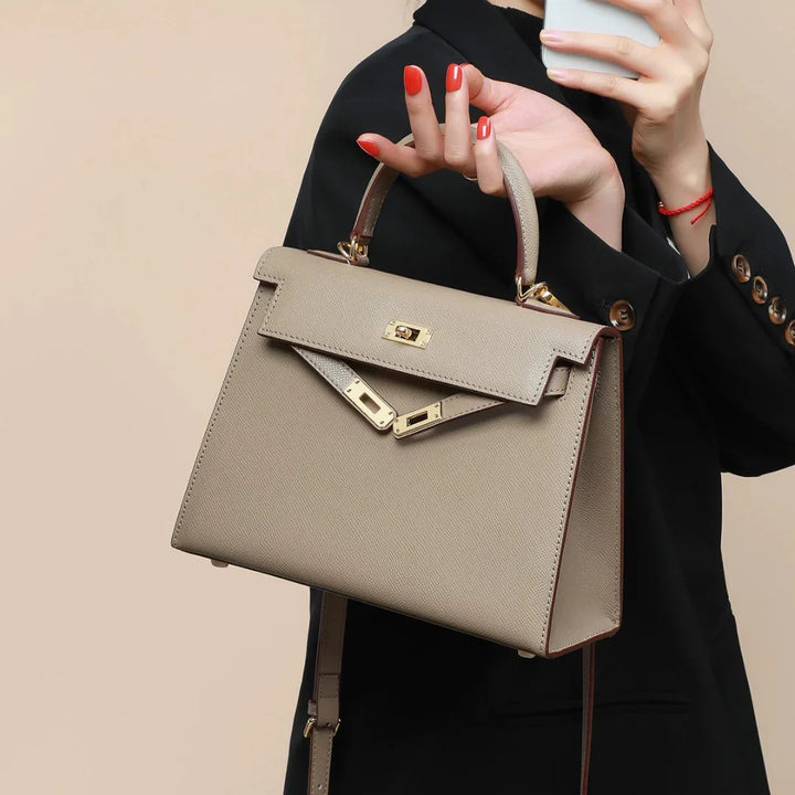 Stylish beige structured women's shoulder bag with a refined top handle and functional turn lock closure.